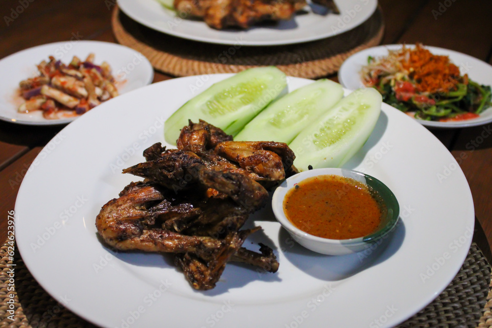 Ayam taliwang or taliwang chicken, a traditional roasted chicken dish from Lombok usually served with beberuk and water spinach plecing. Served with white plate on a wood background