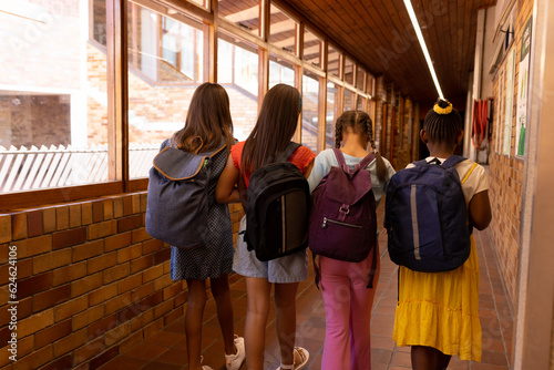 Diverse schoolgirls wearing school bags and walking at school corridor