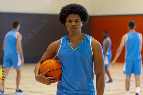 Portrait of biracial male basketball player wearing blue sports clothes over teammates at gym © WavebreakMediaMicro
