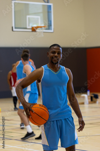 Portrait of happy diverse male basketball players holding and playing basketball at gym