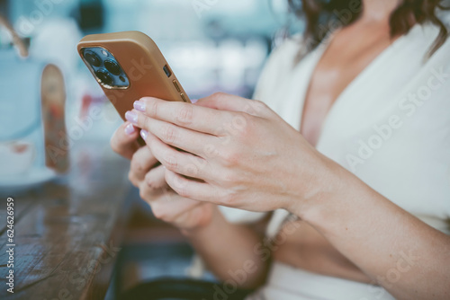 young cute woman using phone,sitting at a cafe holding a smartphone,answering texts,phone calls,letters,posts photos in instagram,outdoor portrait, close up, elaborated and bracelets on the hands
