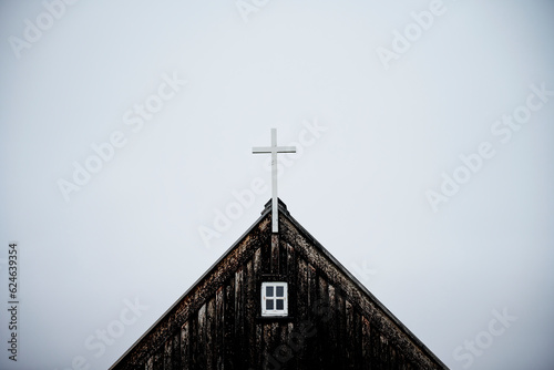 Weathered wooden church with cross on roof against overcast sky photo