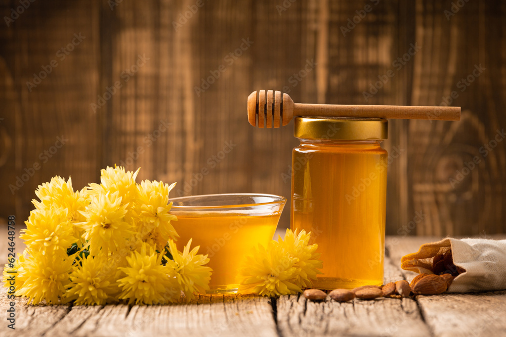 Honey in a glass jar and a bowl, dipper and nuts on a wooden background Honey in a glass jar and a bowl, dipper and nuts on a wooden background