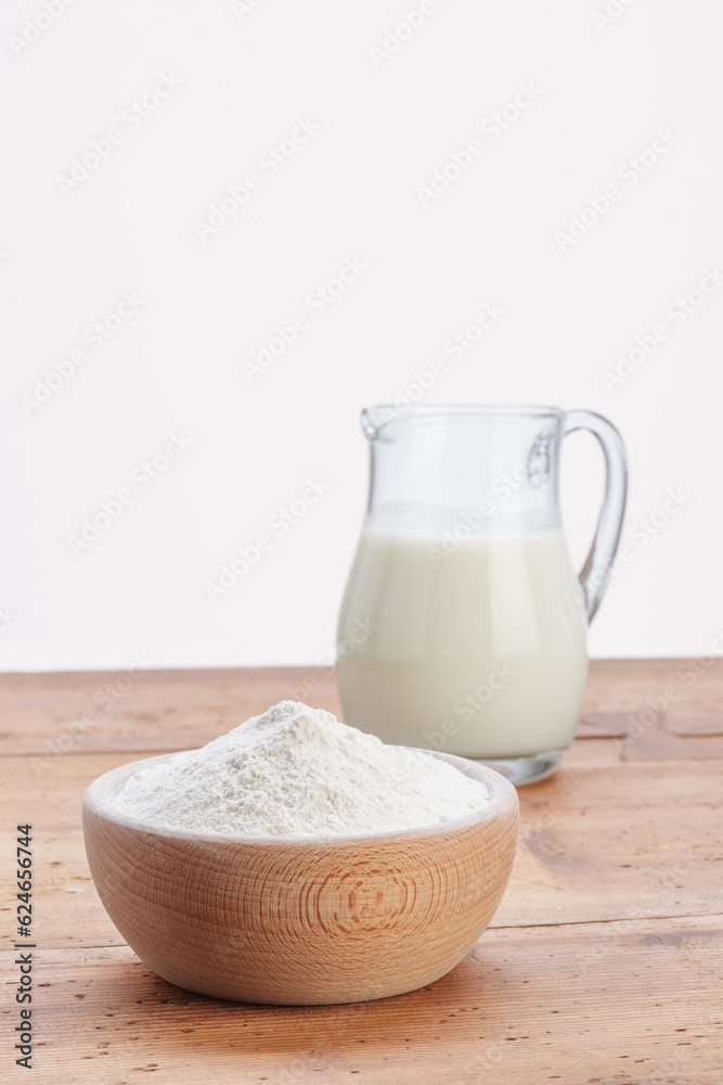 glass jug with wooden bowl full of white flour, on rustic wooden table glass jug with wooden bowl full of white flour, on rustic wooden table
