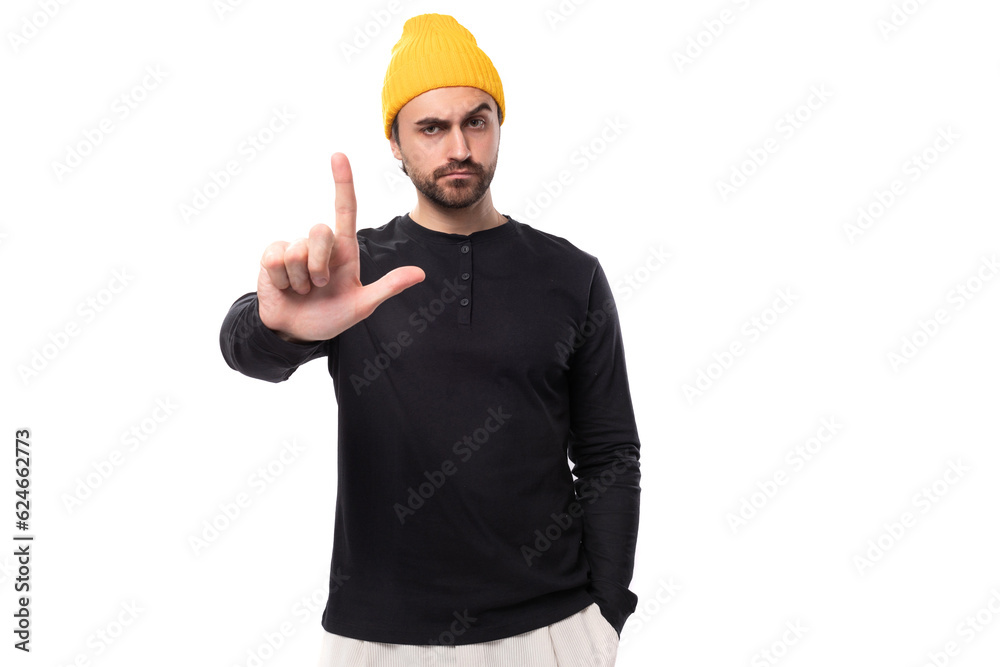 young brunette confident male model with a beard dressed in a black jacket and a yellow hat