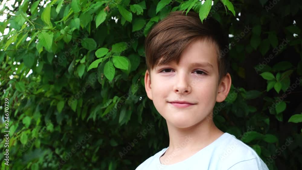 a ten-year-old boy looks into the camera against the background of green leaves of a bush. a ten-year-old boy looks into the camera against the background of green leaves of a bush.