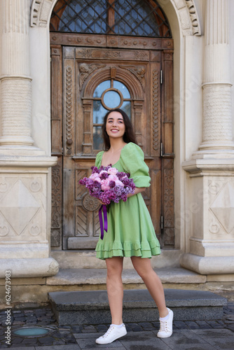 Beautiful woman with bouquet of spring flowers near building outdoors © New Africa