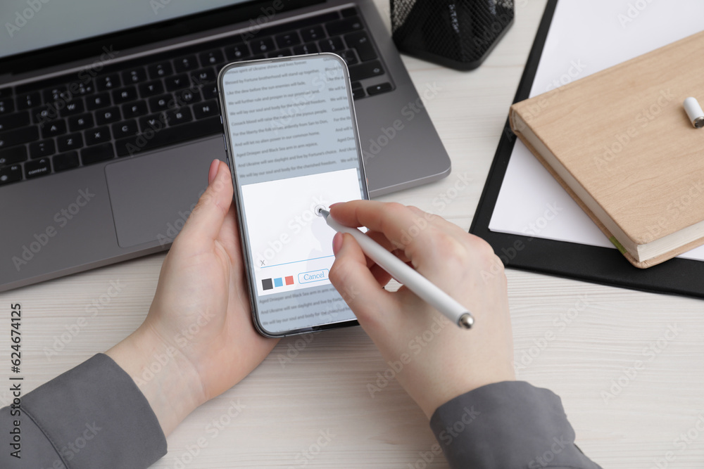 Fototapeta premium Electronic signature. Woman using stylus and mobile phone at white wooden table, closeup