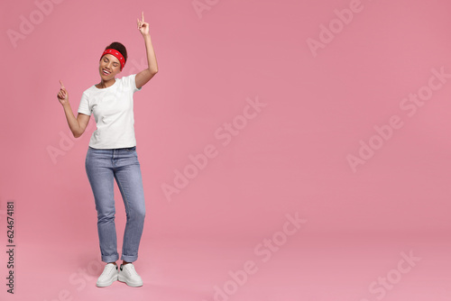 Happy young woman in stylish headband dancing on pink background. Space for text