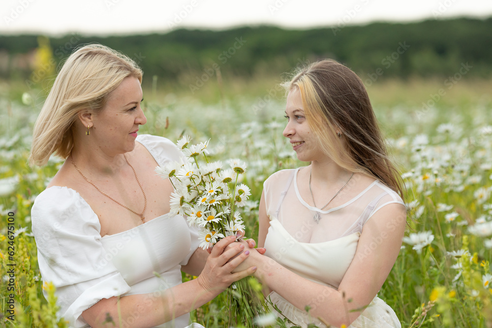 Family on nature on a summer sunny day. Mom with a daughter in a chamomile field. Mom and daughter look at each other and smile. Mom with daughter in white dresses. Image with selective focus. Family on nature on a summer sunny day. Mom with a daughter in a chamomile field. Mom and daughter look at each other and smile. Mom with daughter in white dresses. Image with selective focus.