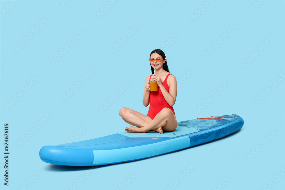 Happy woman with refreshing drink resting on SUP board against light blue background Happy woman with refreshing drink resting on SUP board against light blue background
