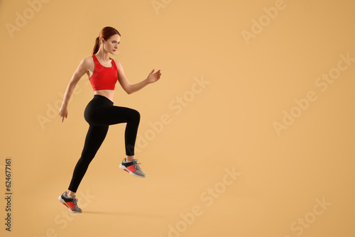 Young woman in sportswear running on beige background, space for text