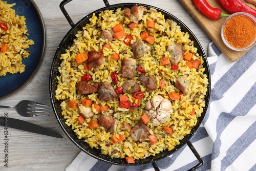 Delicious pilaf with meat, carrot and chili pepper served on wooden table, flat lay