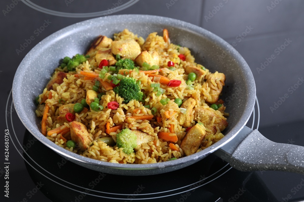 Tasty rice with meat and vegetables in frying pan on induction stove, closeup