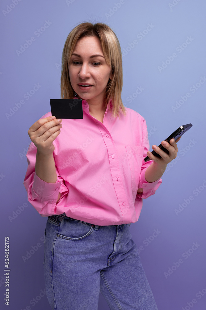 young blond european office worker lady with flowing hair in a pink blouse pays for purchases using a card and phone young blond european office worker lady with flowing hair in a pink blouse pays for purchases using a card and phone