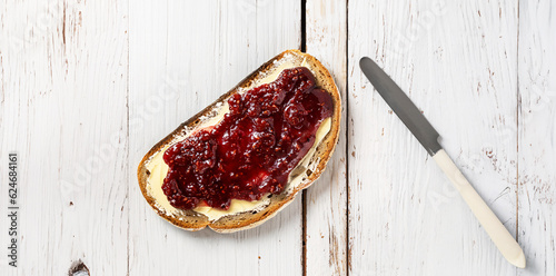 illustrazione con fetta di pane integrale imburrato e marmellata su tavola in legno grezzo verniciata di bianco, coltello, vista dall'alto, Generative Ai photo