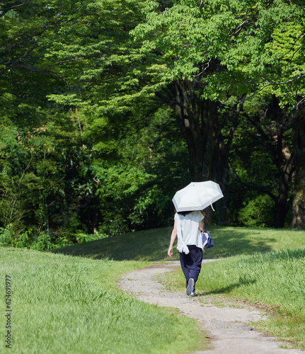 真夏の公園で日傘を持って散歩している若い女性の後姿