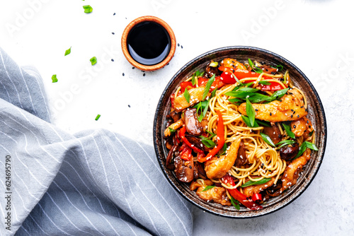 Photo Stir fry noodles with chicken slices, red paprika, mushrooms, chives, soy sauce and sesame seeds in ceramic bowl