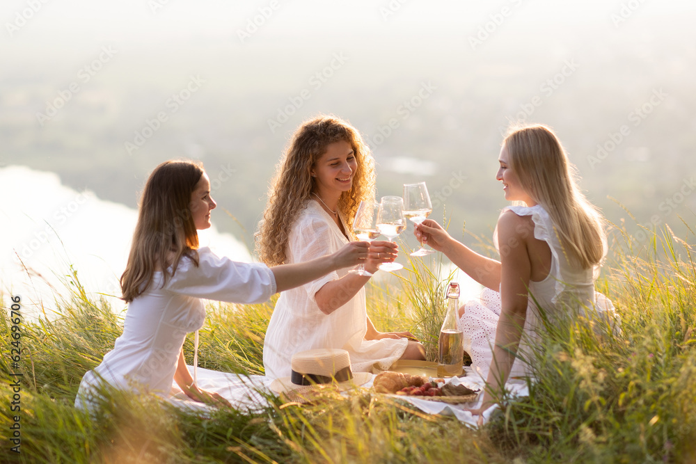 Summertime. Young happy girlfriends enjoyed picnic day on the hill at sunset. Lifestyle, vacation concept