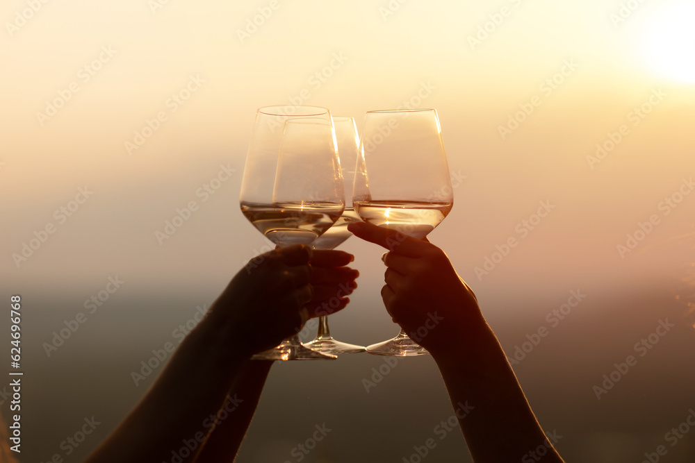 Friends clinking glasses with wine and enjoying wine against a beautiful sunset.
