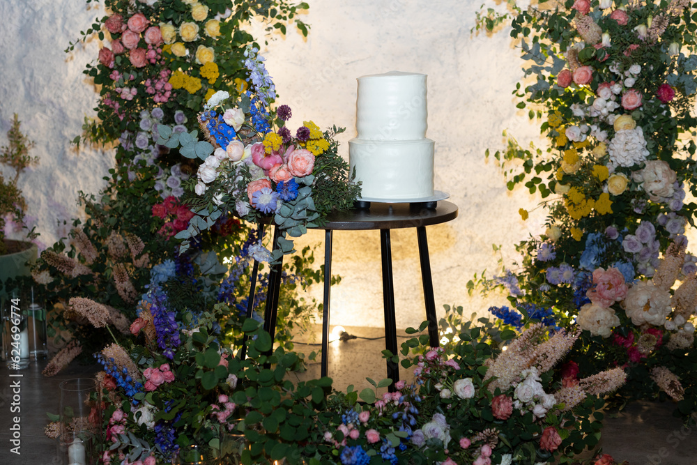 White wedding cake in the evening. Cake on the background of an arch of fresh flowers.