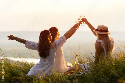 Lovely ladies drinking wine at sunset. Summer happy mood. Girlfriends relaxing on summer sunset with river on the background. 