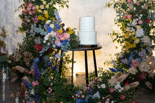 Obraz na płótnie White wedding cake in the evening. Cake on the background of an arch of fresh flowers. w salonie