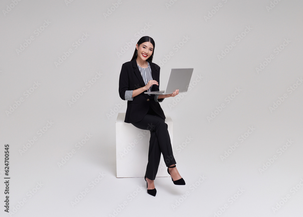 Young businesswoman asian happy smiling. While her using laptop sitting on white chair isolated on copy space white studio background.