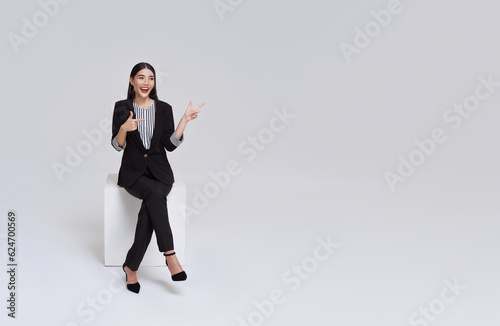 Young Asian businesswoman in suit sitting and pointing to empty copy space isolated on white background.