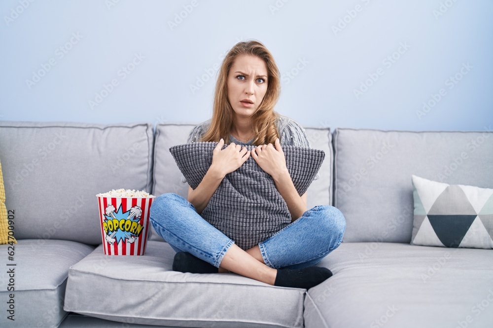 Beautiful blonde woman watching tv sitting on the sofa clueless and confused expression. doubt concept. Beautiful blonde woman watching tv sitting on the sofa clueless and confused expression. doubt concept.