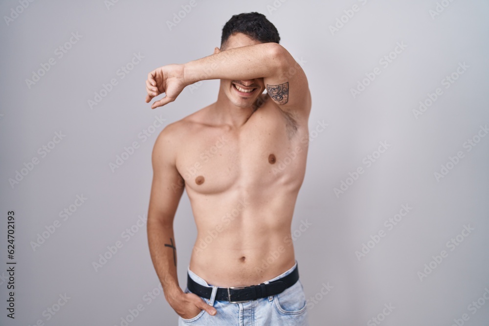 Handsome hispanic man standing shirtless smiling cheerful playing peek a boo with hands showing face. surprised and exited