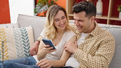 Man and woman couple using smartphone sitting on sofa at home