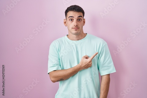 Handsome hispanic man standing over pink background pointing aside worried and nervous with forefinger, concerned and surprised expression