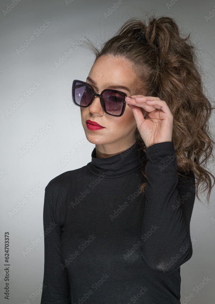 Woman with sunglasses  and black blouse against a grey background. Style beauty girl with red lips.Portrait of stunning young woman in sunglasses look into the camera