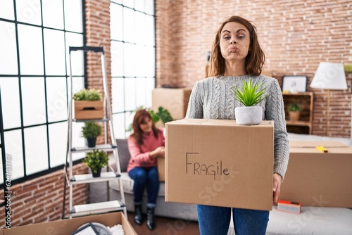 Mother and daughter moving to a new home holding cardboard box puffing cheeks with funny face. mouth inflated with air, catching air. © Krakenimages.com