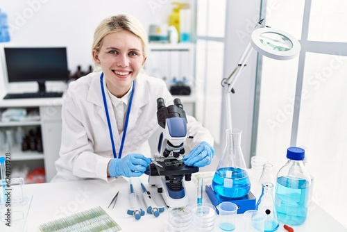 Fototapeta Naklejka Na Ścianę i Meble -  Young blonde woman scientist using microscope smiling at laboratory