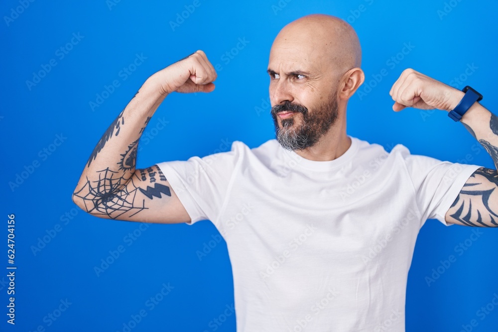 Hispanic man with tattoos standing over blue background showing arms muscles smiling proud. fitness concept. Hispanic man with tattoos standing over blue background showing arms muscles smiling proud. fitness concept.