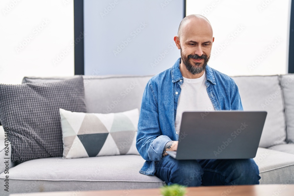 Young bald man using laptop sitting on sofa at home Young bald man using laptop sitting on sofa at home