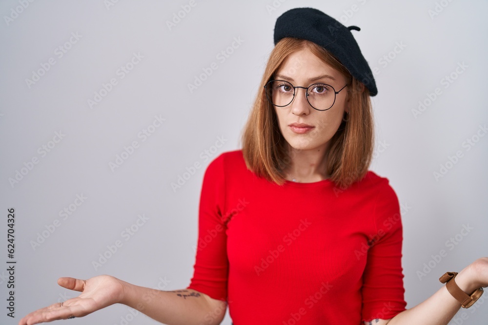 Young redhead woman standing wearing glasses and beret clueless and confused with open arms, no idea concept. Young redhead woman standing wearing glasses and beret clueless and confused with open arms, no idea concept.