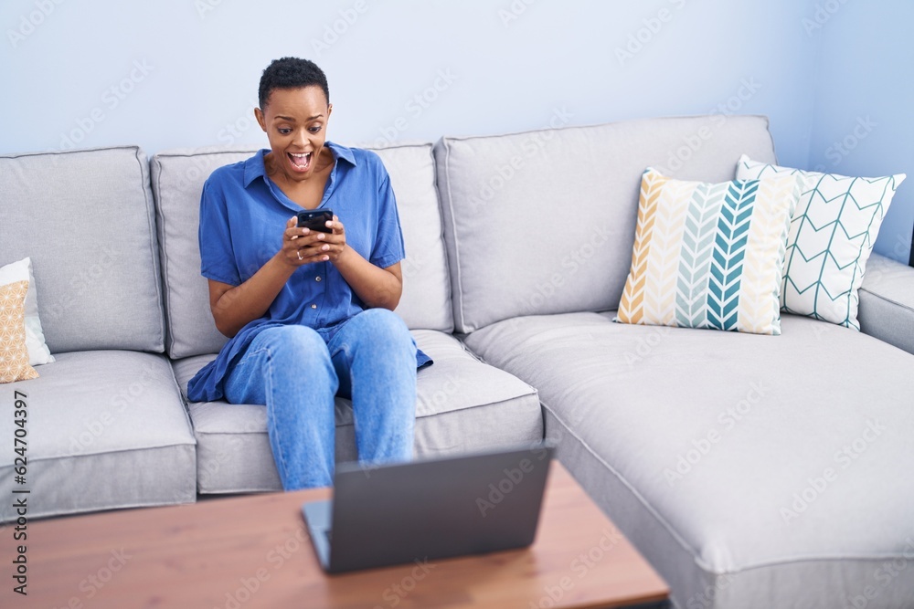 African american woman using smartphone sitting on sofa at home African american woman using smartphone sitting on sofa at home