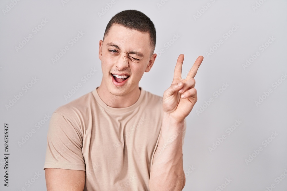 Young man standing over isolated background smiling with happy face winking at the camera doing victory sign with fingers. number two. Young man standing over isolated background smiling with happy face winking at the camera doing victory sign with fingers. number two.