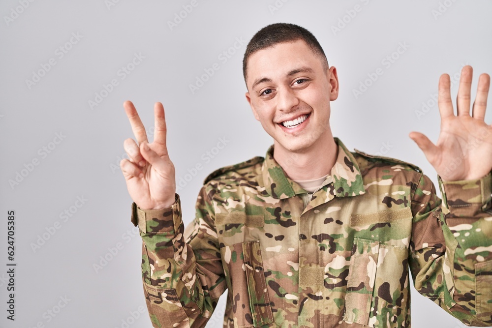 Young man wearing camouflage army uniform showing and pointing up with fingers number seven while smiling confident and happy. Young man wearing camouflage army uniform showing and pointing up with fingers number seven while smiling confident and happy.