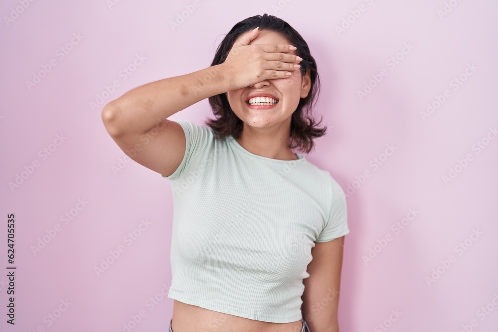 Hispanic young woman standing over pink background smiling and laughing with hand on face covering eyes for surprise. blind concept. Hispanic young woman standing over pink background smiling and laughing with hand on face covering eyes for surprise. blind concept.