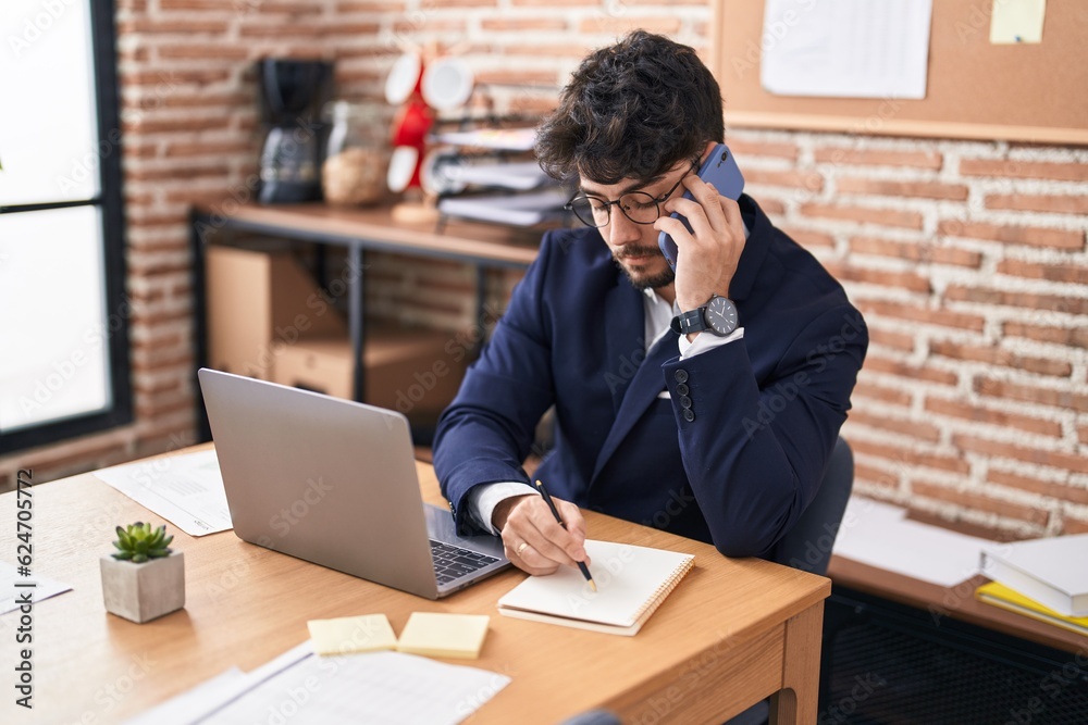 Young hispanic man business worker talking on smartphone write on notebook at office Young hispanic man business worker talking on smartphone write on notebook at office