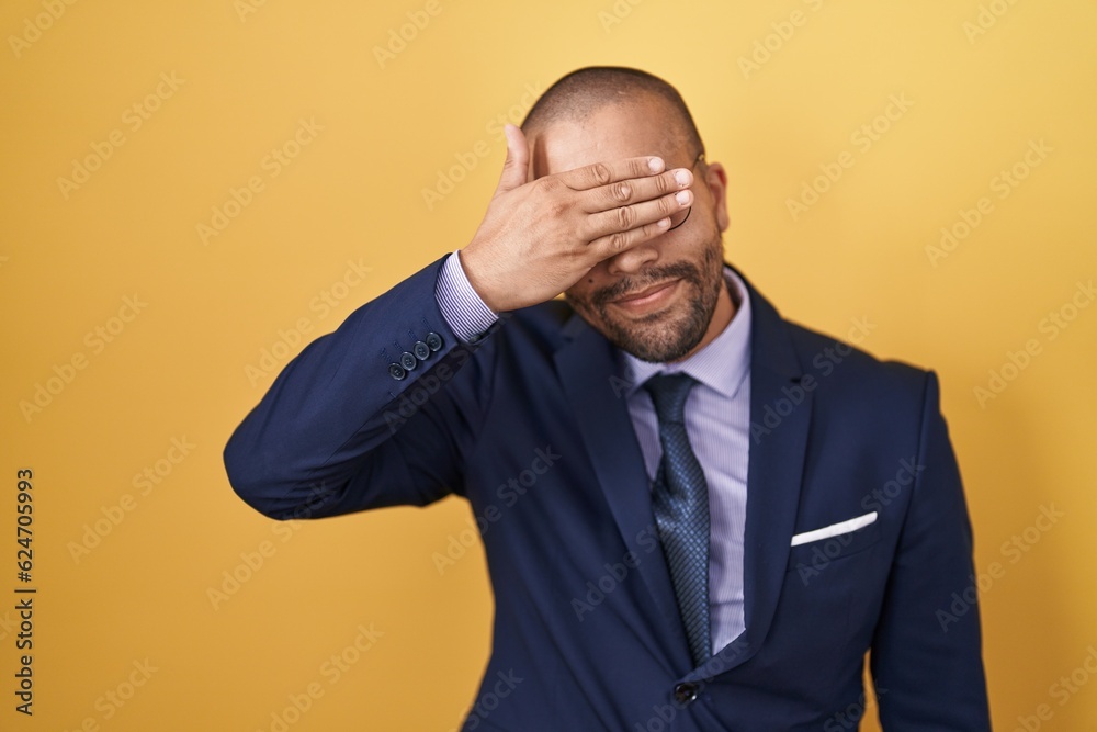 Hispanic man with beard wearing suit and tie smiling and laughing with hand on face covering eyes for surprise. blind concept. Hispanic man with beard wearing suit and tie smiling and laughing with hand on face covering eyes for surprise. blind concept.