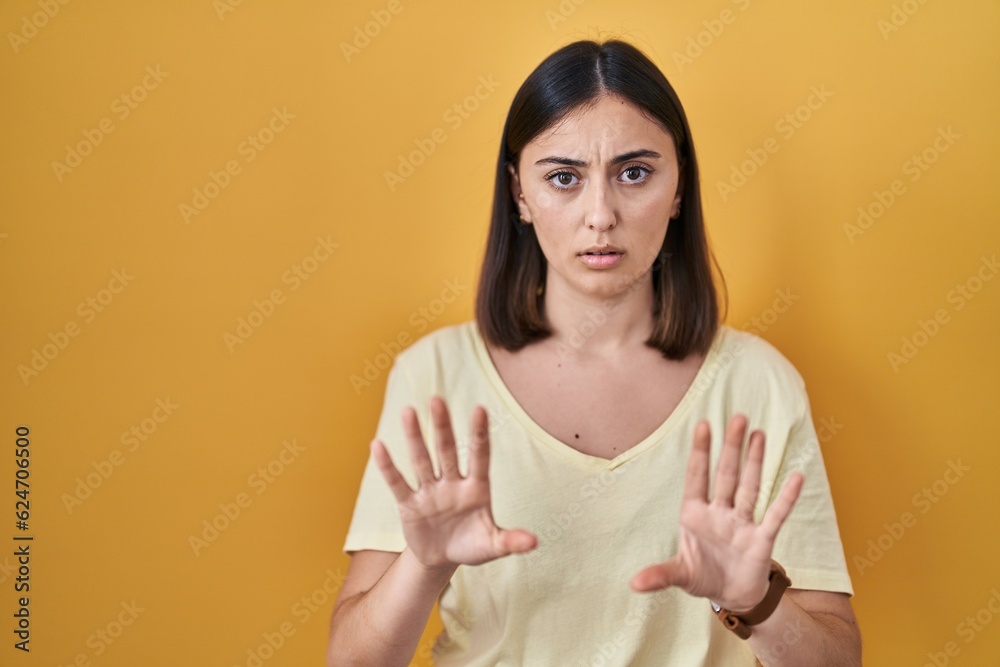 Obraz premium Hispanic girl wearing casual t shirt over yellow background moving away hands palms showing refusal and denial with afraid and disgusting expression. stop and forbidden.