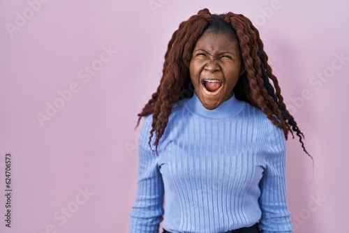 African woman standing over pink background angry and mad screaming frustrated and furious, shouting with anger. rage and aggressive concept. © Krakenimages.com