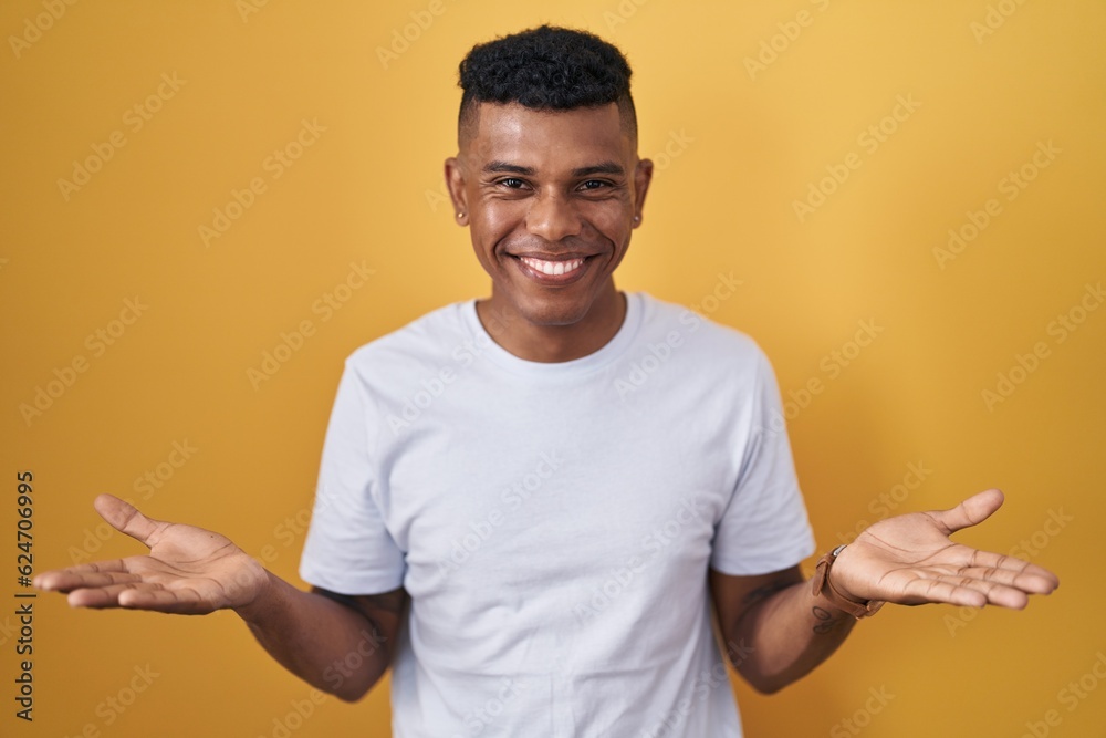 Young hispanic man standing over yellow background smiling cheerful with open arms as friendly welcome, positive and confident greetings Young hispanic man standing over yellow background smiling cheerful with open arms as friendly welcome, positive and confident greetings