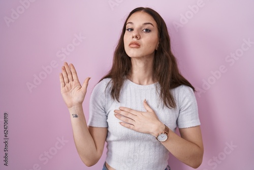 Young hispanic girl standing over pink background swearing with hand on chest and open palm, making a loyalty promise oath