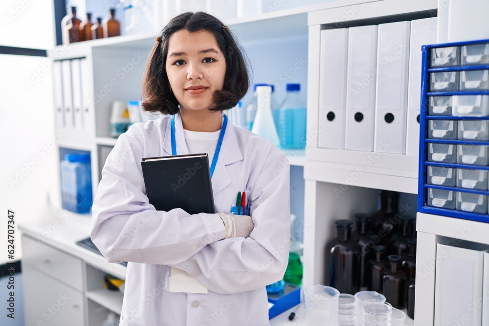 Young hispanic woman working at scientist laboratory relaxed with serious expression on face. simple and natural looking at the camera.